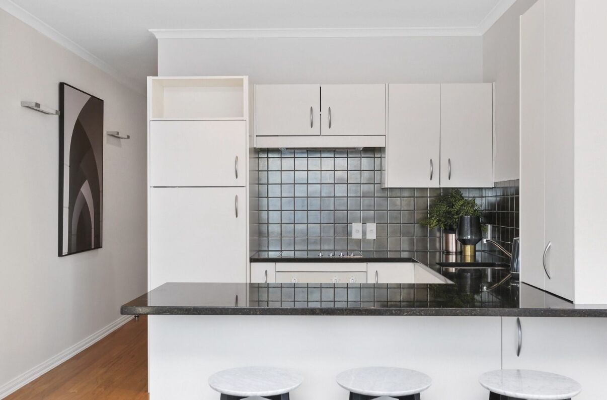 A modern kitchen with white cabinets, a black countertop, and a tiled backsplash.