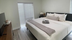 A bedroom with a bed, bedside table, lamp, and a window with blinds. - Updated 2-Bedroom with a pool and hot tub (Columbus)