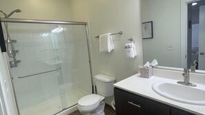 A modern bathroom with a glass shower enclosure, a white toilet, a vanity with a sink, and a mirror above the sink. - Updated 2-Bedroom with a pool and hot tub (Columbus)