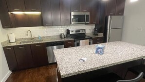 A modern kitchen with dark wooden cabinets, stainless steel appliances, a granite countertop, and pendant lighting.