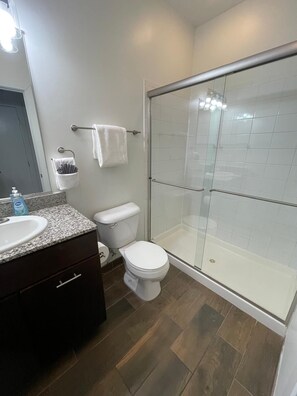 Un baño moderno con lavamanos de granito, inodoro y ducha con mampara de vidrio.