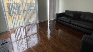 A spacious living room with a dark leather sofa, a ceiling fan, and a large sliding glass door leading to an outdoor area.