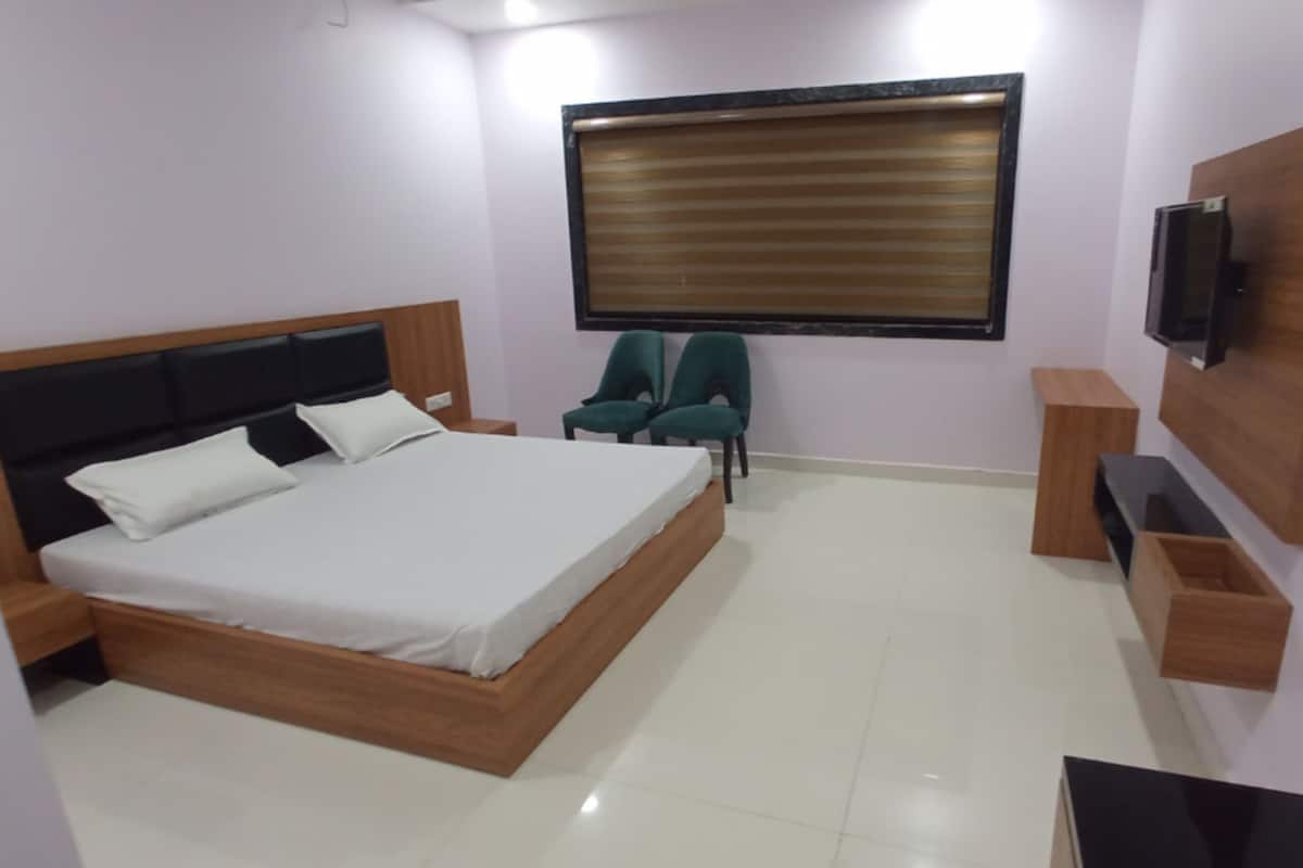 A bedroom with a wooden bed, a TV mounted on the wall, and two green chairs.