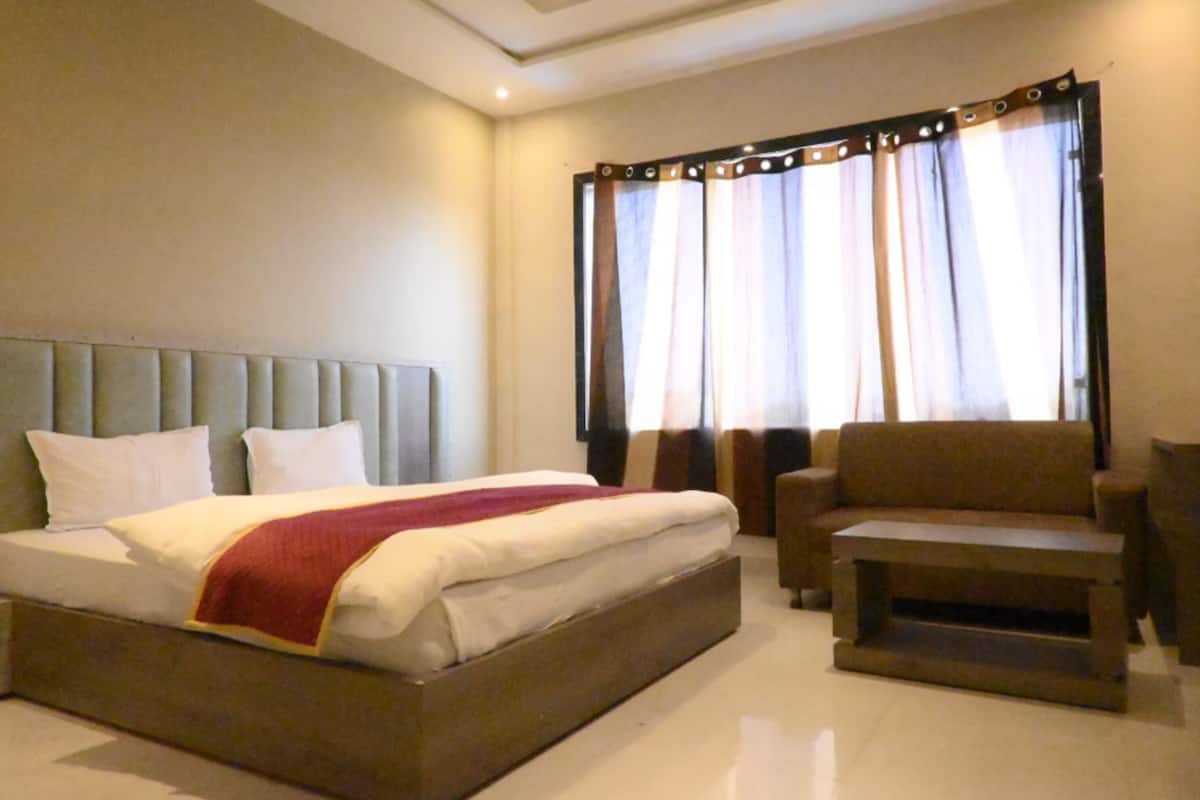 A hotel room with a bed, a sofa, a small table, and curtains.