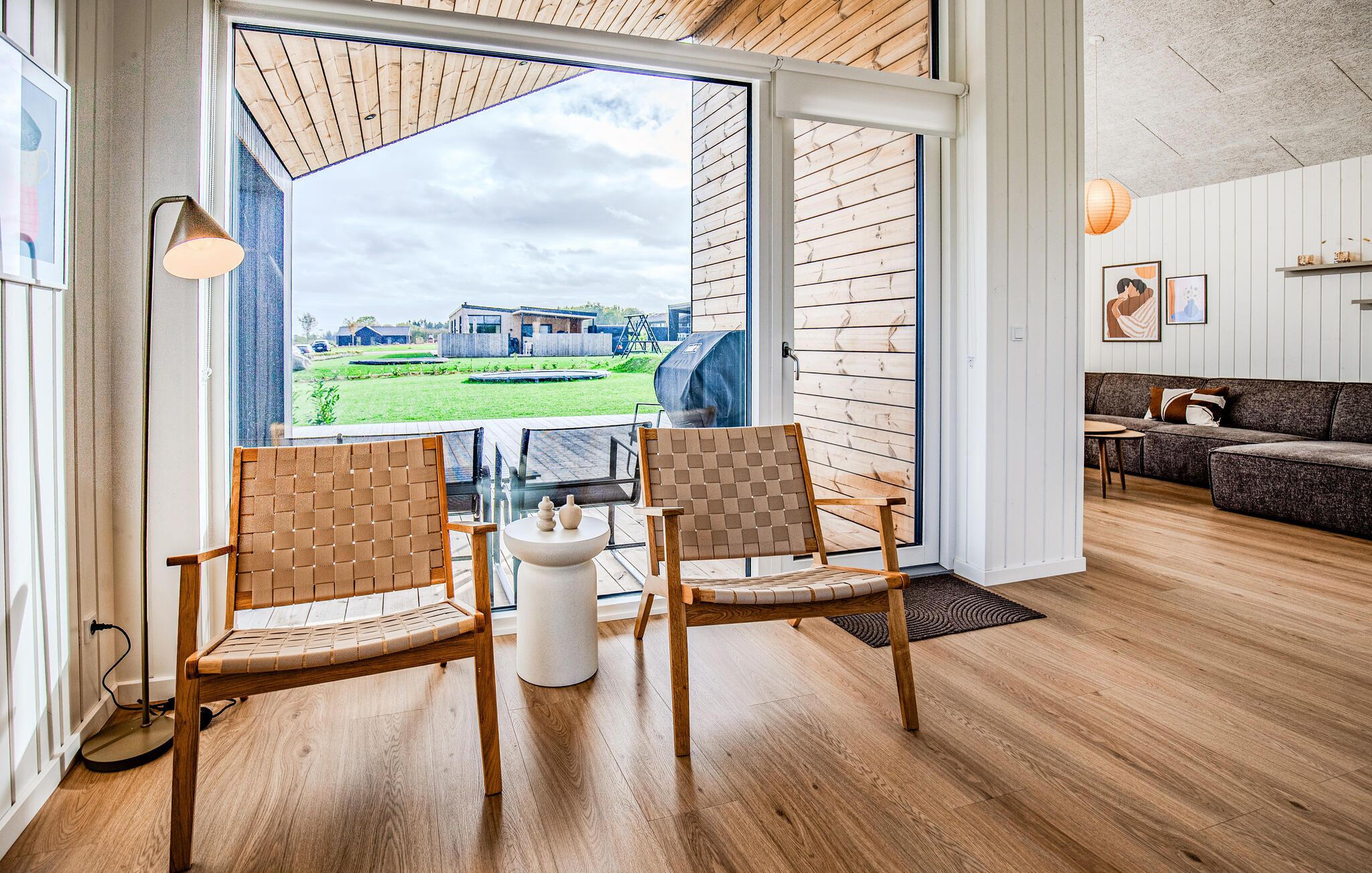 A spacious room with a large sliding glass door leading to an outdoor area, two wooden chairs, a small white table, and a sofa.