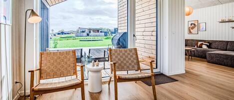 A spacious room with a large sliding glass door leading to an outdoor area, two wooden chairs, a small white table, and a sofa.