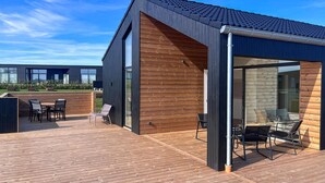 A modern building with a wooden deck, outdoor seating, and a glass enclosure. - Gorgeous home in Børkop with sauna (Børkop)