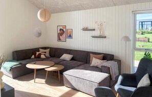 A modern living room with a sectional sofa, two round coffee tables, a side table, and a chair. There are wall-mounted shelves with decorative items and a large window providing a view of the outdoors. - Gorgeous home in Børkop with sauna (Børkop)