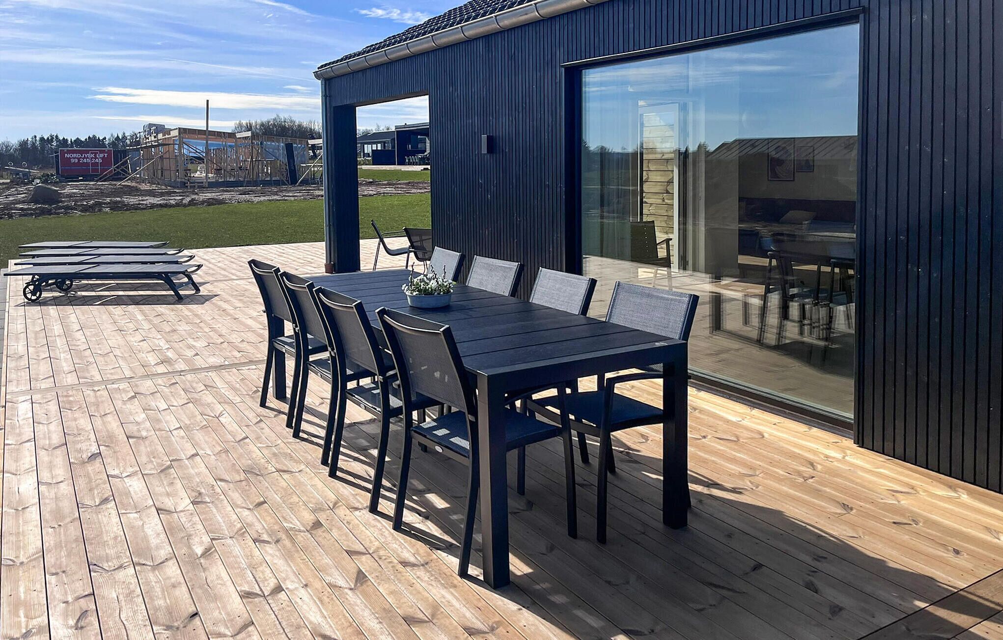 An outdoor patio with a wooden deck, a table with chairs, and a modern building with large windows.