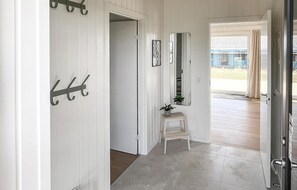 Un couloir avec un porte-manteau, une petite table sur laquelle est posée une plante, un miroir et une porte donnant sur une autre pièce.
