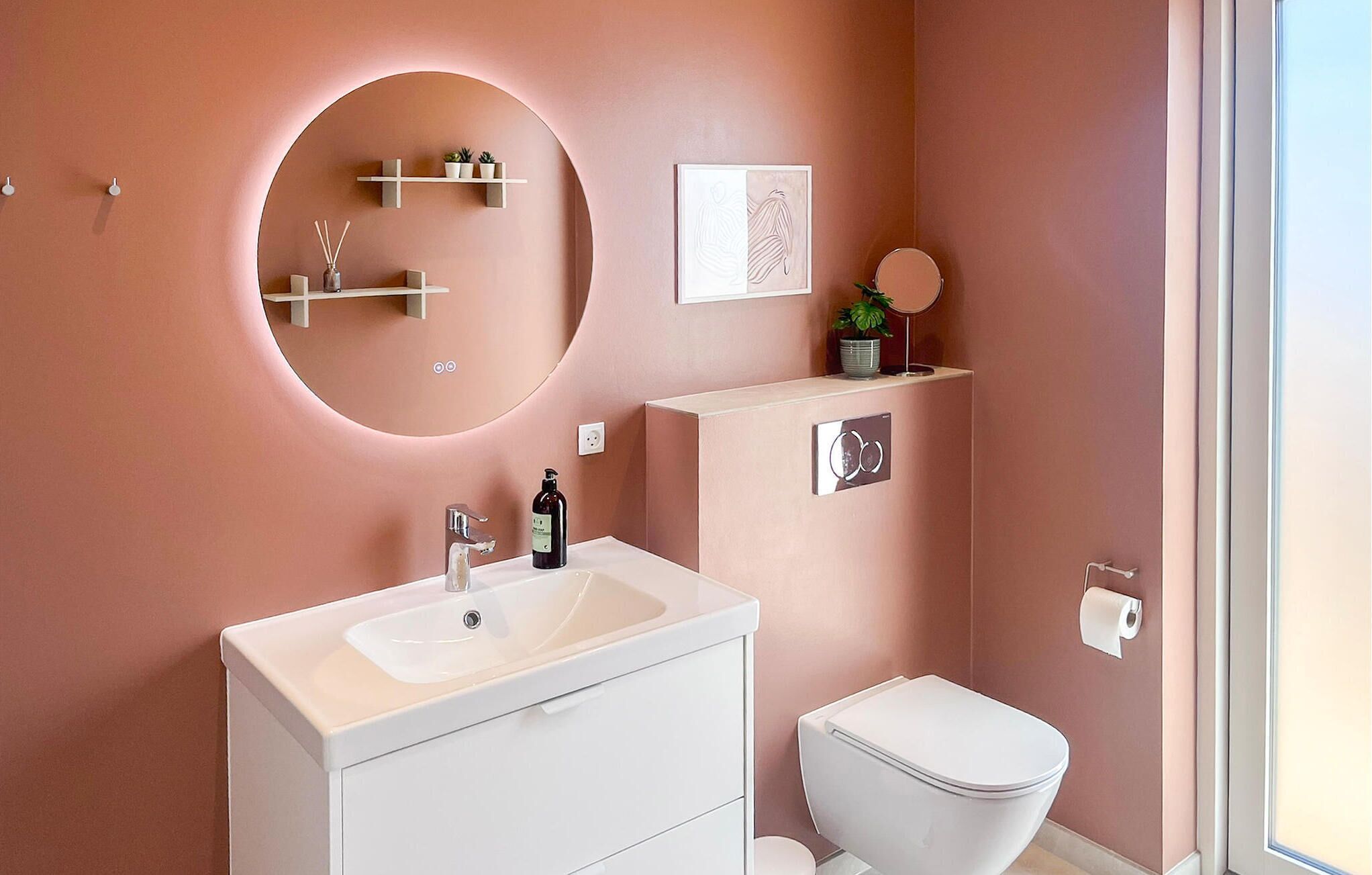 Ein modernes Badezimmer mit rundem Spiegel, weißem Waschtisch und Toilette.