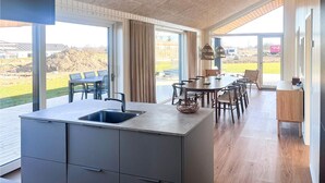 A modern kitchen with a large island, a dining area with chairs, and large windows offering a view of the outdoors. - Gorgeous home in Børkop with sauna (Børkop)