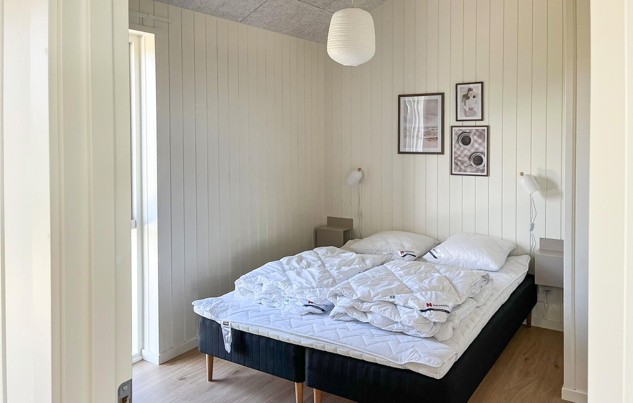 Una cama con ropa blanca, una mesita de noche, una lámpara y decoración en la pared.