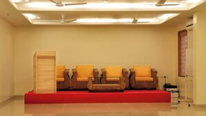 A reception area with four wicker chairs with yellow cushions, a wooden cabinet, and a red carpet. - Hotel Rithanns (Sulur)