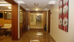 A hallway with a polished marble floor, a wooden door frame, and a wall with a floral painting. - Hotel Rithanns (Sulur)