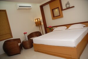 A neatly arranged bedroom with a wooden bed, a small bedside table with a vase of flowers, a chair, and a wall-mounted air conditioner.