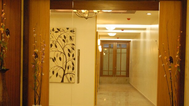 A hotel lobby with a polished marble floor, wooden paneling, and two vases with flowers. - Hotel Rithanns (Sulur)