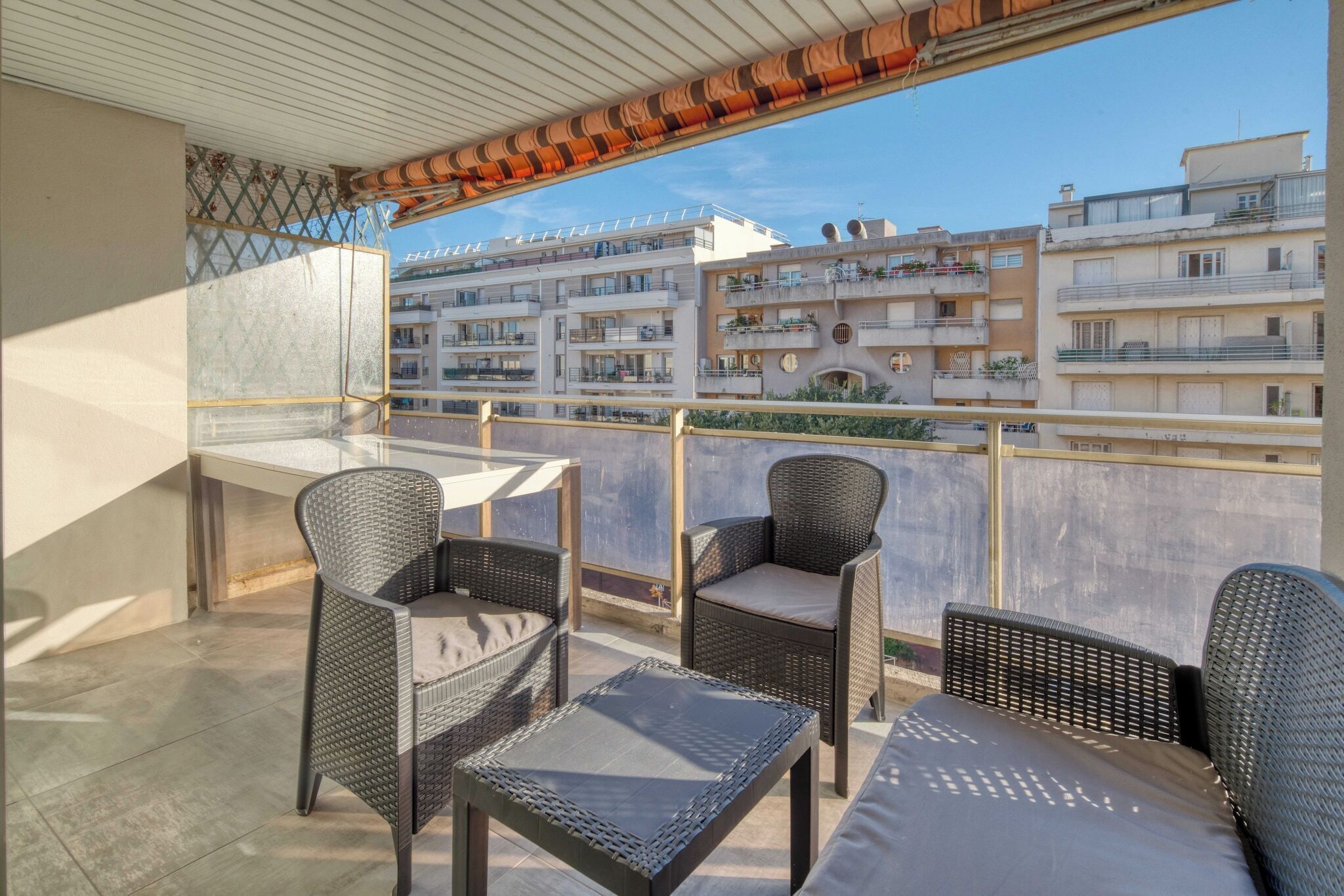 Varanda com mobiliário de vime, piso de azulejos e vista para edifícios altos.