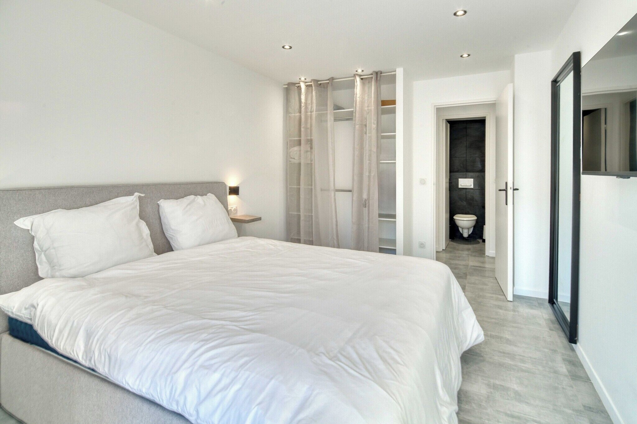 Ein modernes Schlafzimmer mit einem großen Bett, einem Nachttisch, einem Kleiderschrank und einem durchgehenden Türspalte sichtbaren Badezimmer.