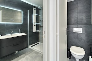 Ein modernes Badezimmer mit einer gläsernen Duschkabine, einem weißen Waschbecken mit Spiegel und einer Toilette.
