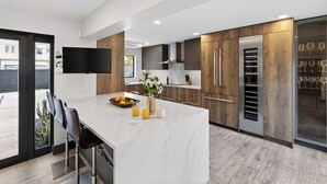 A modern kitchen with a marble island, wooden cabinets, and a built-in wine rack. - Pool + Hot Tub | 5 Min Walk to Beach | Birch Park | Soleil Modern (Fort Lauderdale)