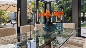A modern dining area with a glass table, beige chairs, and a vase with orange flowers. - Pool + Hot Tub | 5 Min Walk to Beach | Birch Park | Soleil Modern (Fort Lauderdale)