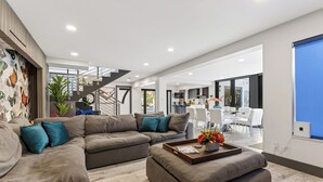 A modern living room with a sectional sofa, a coffee table with a tray, and a staircase leading to an upper floor. - Pool + Hot Tub | 5 Min Walk to Beach | Birch Park | Soleil Modern (Fort Lauderdale)