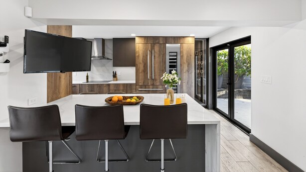 A modern kitchen with a central island, black bar stools, and a large window providing a view of the outdoors. - Pool + Hot Tub | 5 Min Walk to Beach | Birch Park | Soleil Modern (Fort Lauderdale)