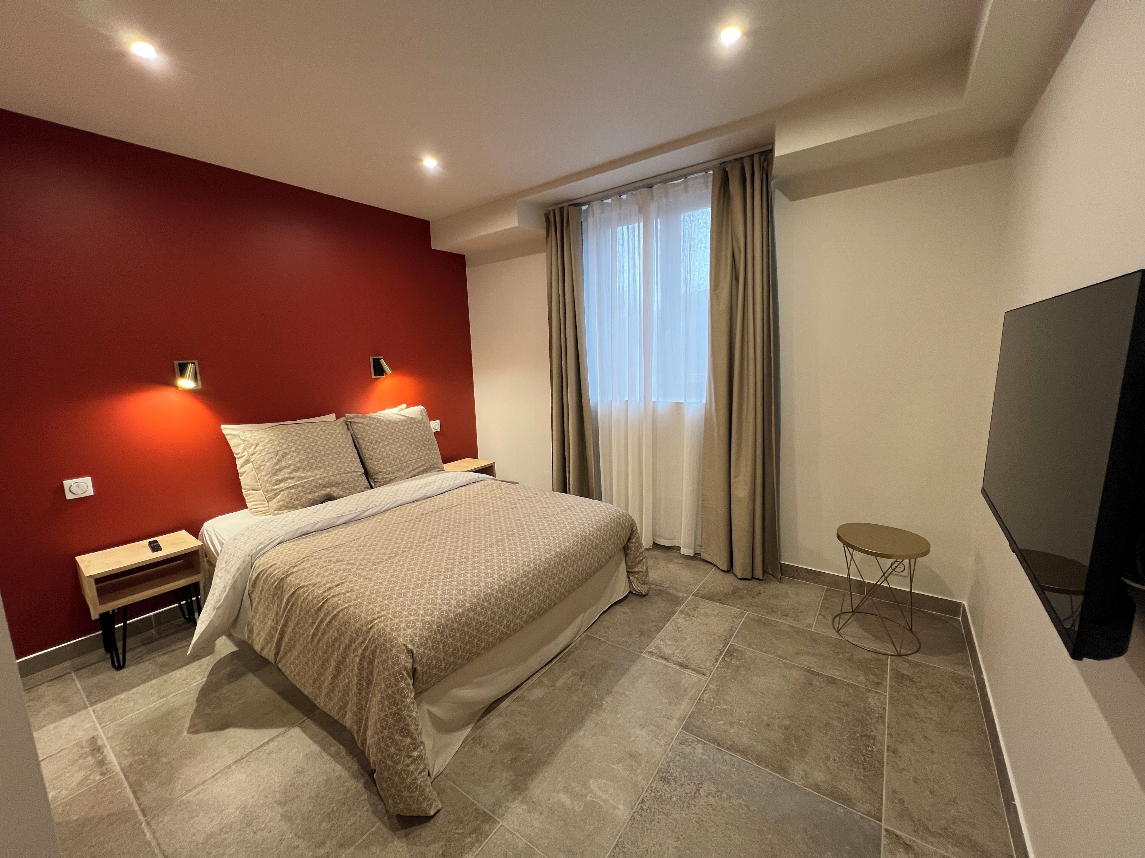 Quarto moderno com uma cama grande, mesas de cabeceira, uma TV e uma janela com cortinas.