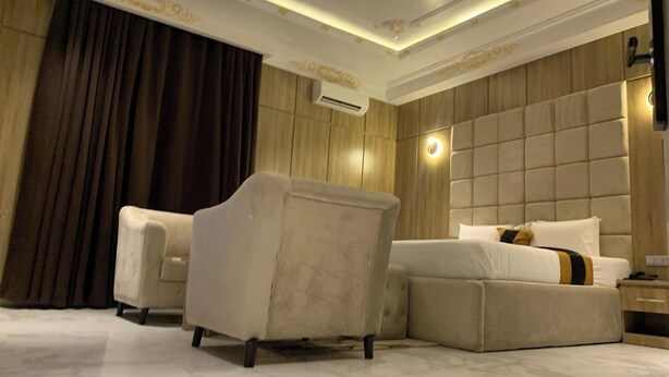 Quarto de hotel com uma cama grande, um sofá, uma poltrona e uma mesa de cabeceira.