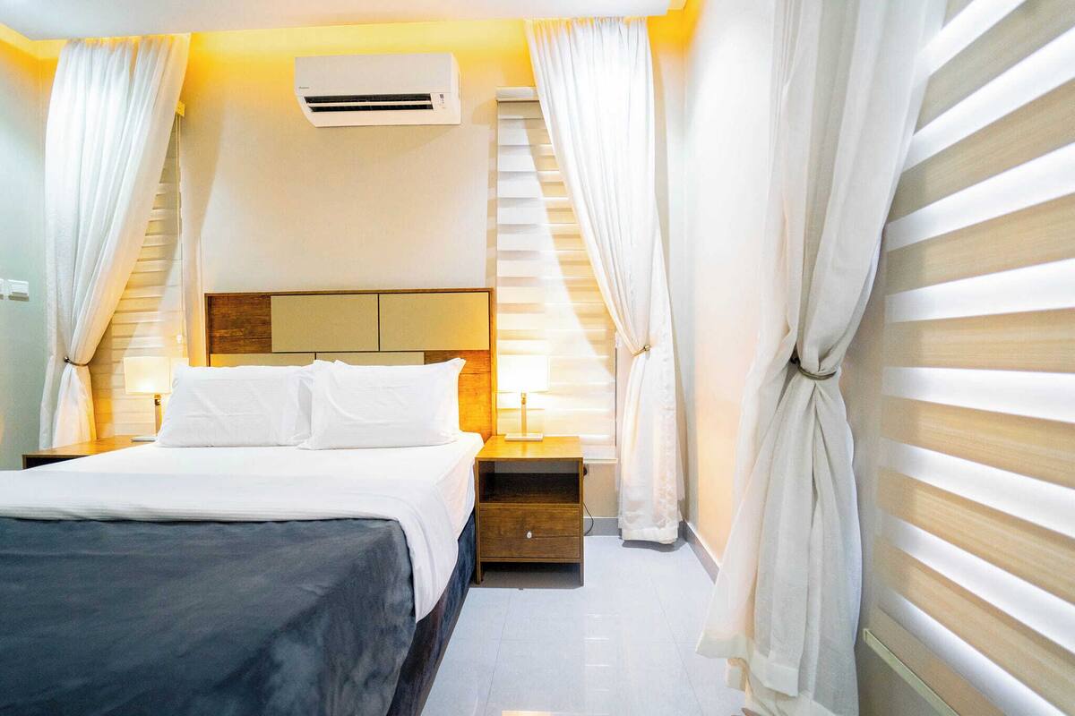 Une chambre d’hôtel comprenant un lit, des tables de chevet, un appareil de climatisation et des rideaux.