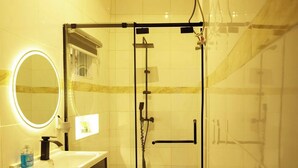 Casa de banho moderna com cabine de duche em vidro, toucador com espelho e dispensador de sabonete, e candeeiro sobre o espelho.