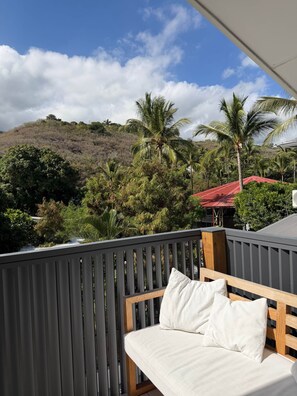 A balcony with a wooden bench and white cushions, overlooking a lush landscape with palm trees and a hill. - Appt Tradition - L'Escale Bleue Saint-Leu, Réunion (Saint-Leu)