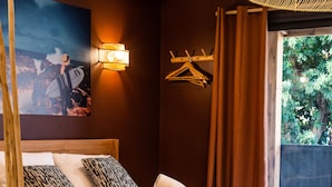 Quarto com cama, almofadas, manta, cabideiro e mesa de jantar com pratos e talheres.