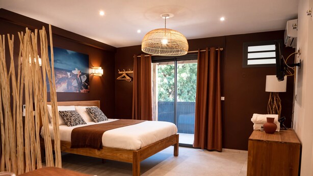 Quarto moderno com cama de madeira, área de refeições com pratos e talheres, uma janela grande com cortinas e ar-condicionado fixado na parede.