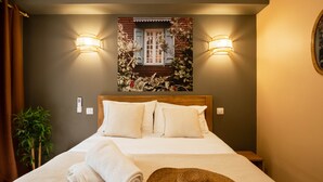 A neatly made bed with a checkered pillowcase, a rolled white towel, and a straw hat on the bed. There are two wall-mounted lights and a framed picture above the bed. - Appt Endémik - L'Escale Bleue Saint-Leu, Reunion Island (Saint-Leu)