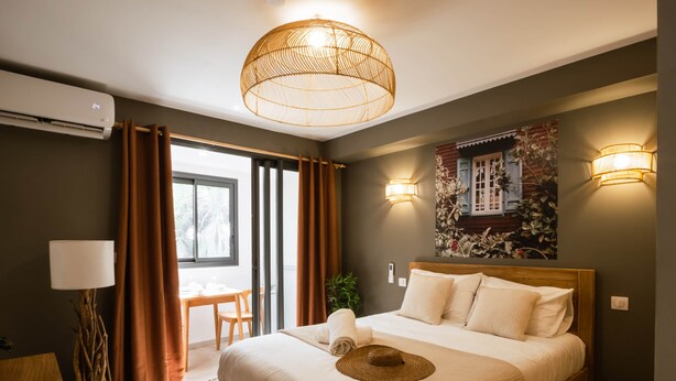 A bedroom with a bed, a table, and a chair, a window with curtains, and wall-mounted lights. - Appt Endémik - L'Escale Bleue Saint-Leu, Reunion Island (Saint-Leu)