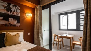 Una camera d'albergo con un letto, un tavolino con sedie, una finestra e un balcone con tende.