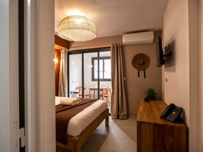 Un dormitorio con cama, escritorio, teléfono, televisor de pared y aire acondicionado.