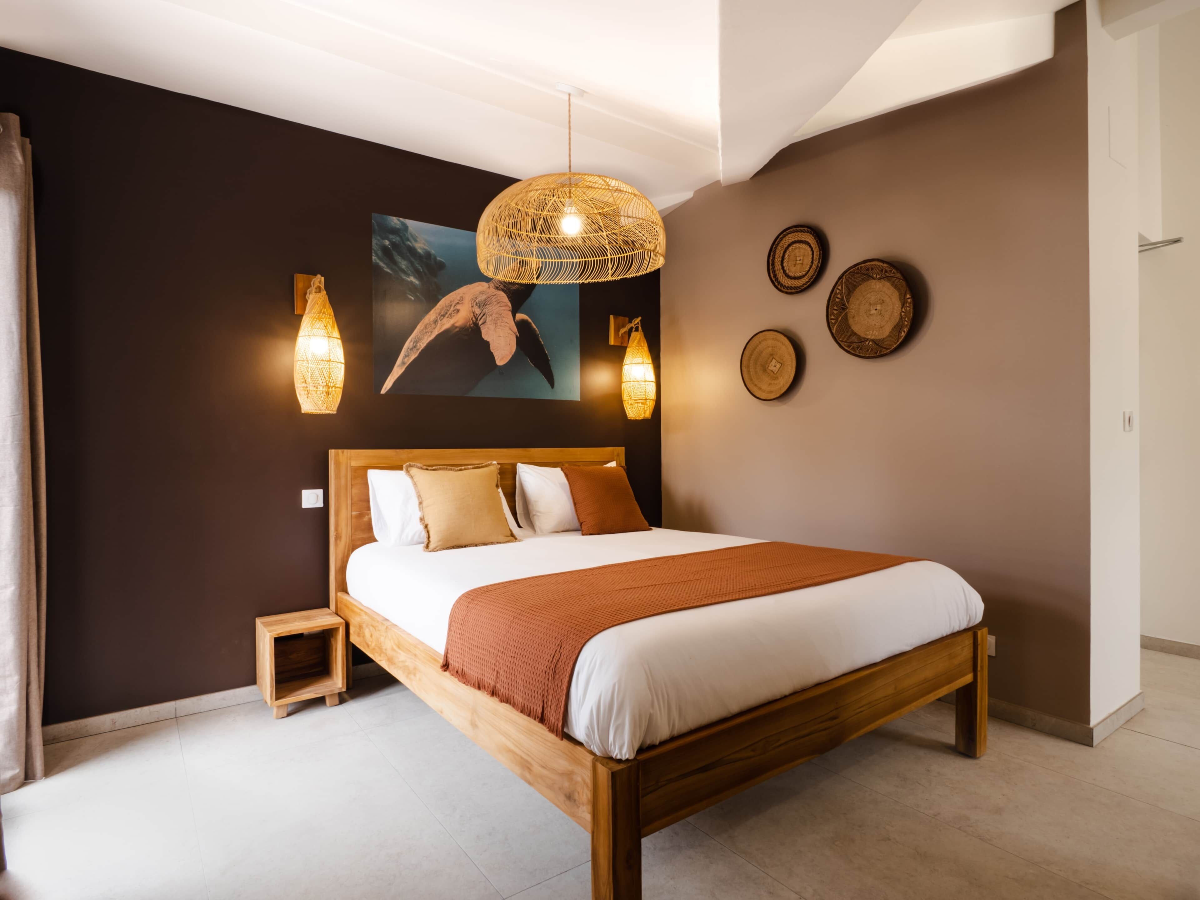 A bedroom with a wooden bed, two bedside tables, a wall-mounted light fixture, and a painting of a bird.