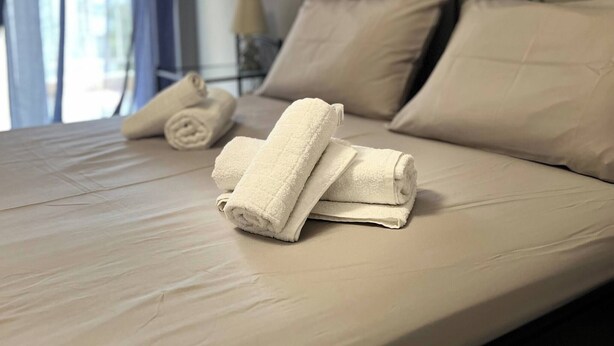Een netjes opgemaakt bed met beige beddengoed en kussens, een zwart metalen hoofdbord en een raam met blauwe gordijnen.