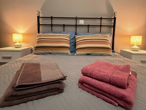 Een net opgemaakt bed met gestreepte kussens, een bruine handdoek gevouwen en een roze handdoek.