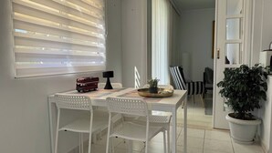 Een eetgedeelte met een witte tafel, twee witte stoelen, een model van een rode dubbeldekkerbus, een zwarte lamp en een plant in pot.