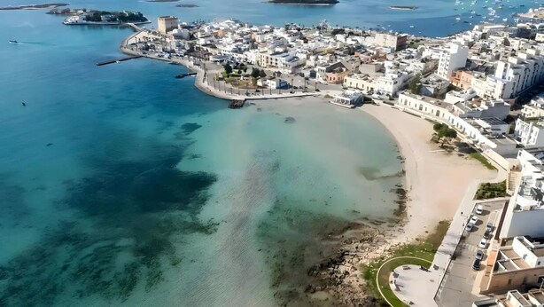 Ett flygbildsbild av en kuststad med en strand, klart vatten och en befäst byggnad.