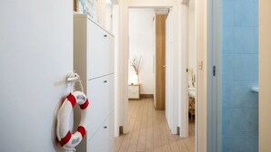 En hall med en vit vägg, en livboj som hänger på väggen och en blå dörr längst ner i hallen.