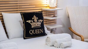 Una cama bien hecha con un cojín negro que tiene una corona y la palabra 'QUEEN'.