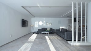 Ein modernes Wohnzimmer mit grauem Sofa, Couchtisch und an der Wand montiertem Fernseher. Drei runde Spiegel sind an der Wand angebracht, und eine Treppe führt auf eine obere Ebene.