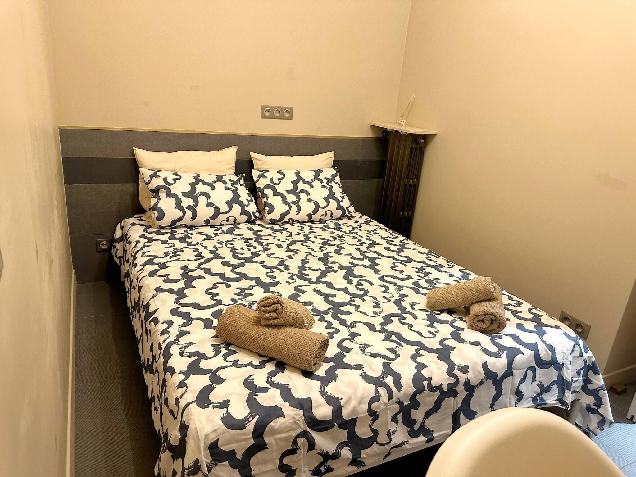 A neatly made bed with a patterned bedspread, two pillows, and two folded towels.