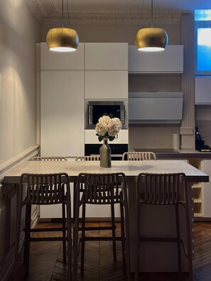 Una cocina moderna con armarios blancos, una isla central con taburetes de bar y dos lámparas colgantes.