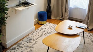En moderne stue med et fladskærms-tv ophængt på væggen, et træsofa-bord, en blå skraldespand og en potteplante.